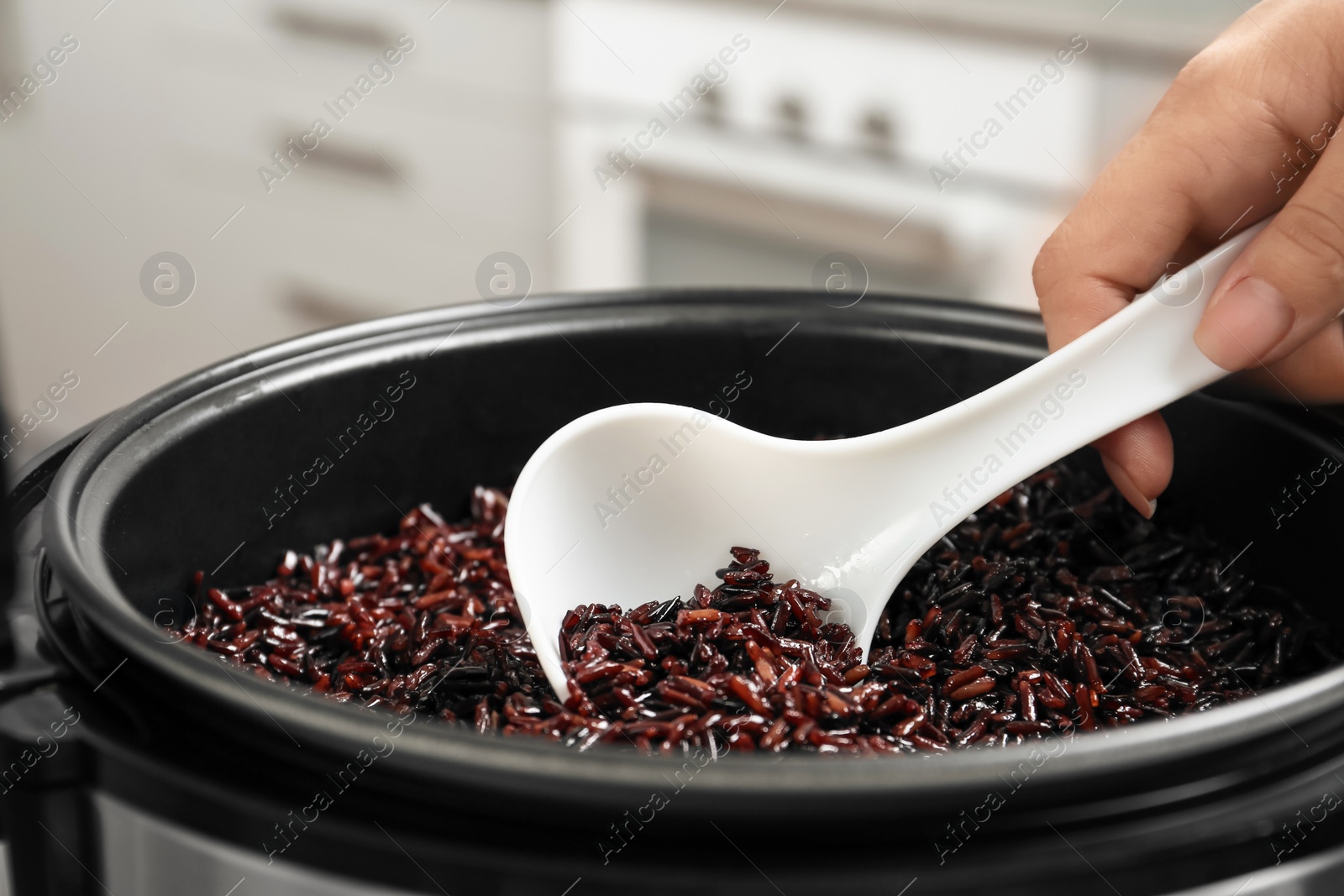 Photo of Woman taking brown rice from multi cooker with spoon in kitchen, closeup