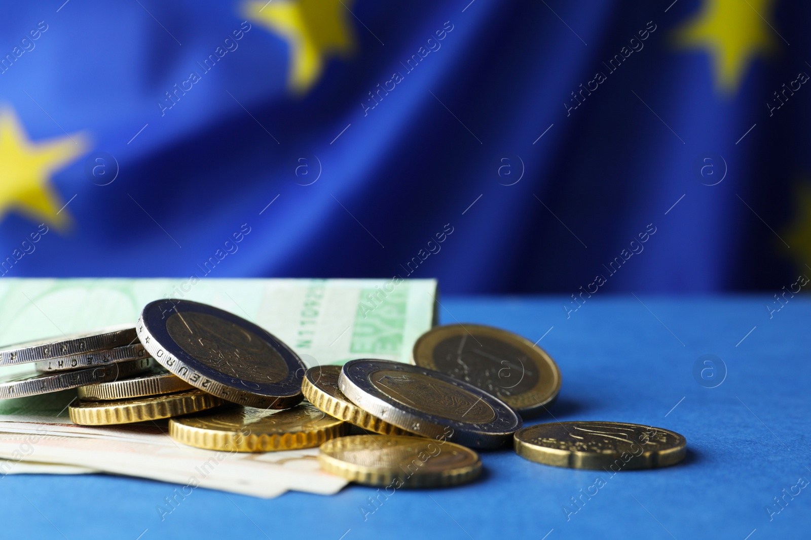 Photo of Coins and banknotes on blue table against European Union flag, closeup. Space for text