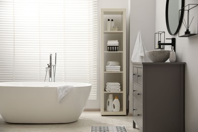 Stylish bathroom interior with grey chest of drawers and shelving unit