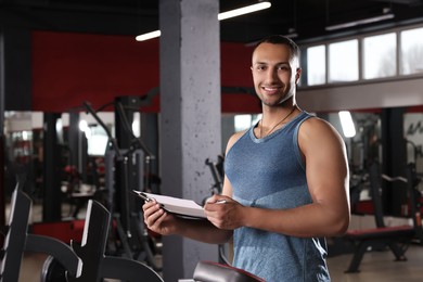 Happy trainer with workout plan in modern gym, space for text