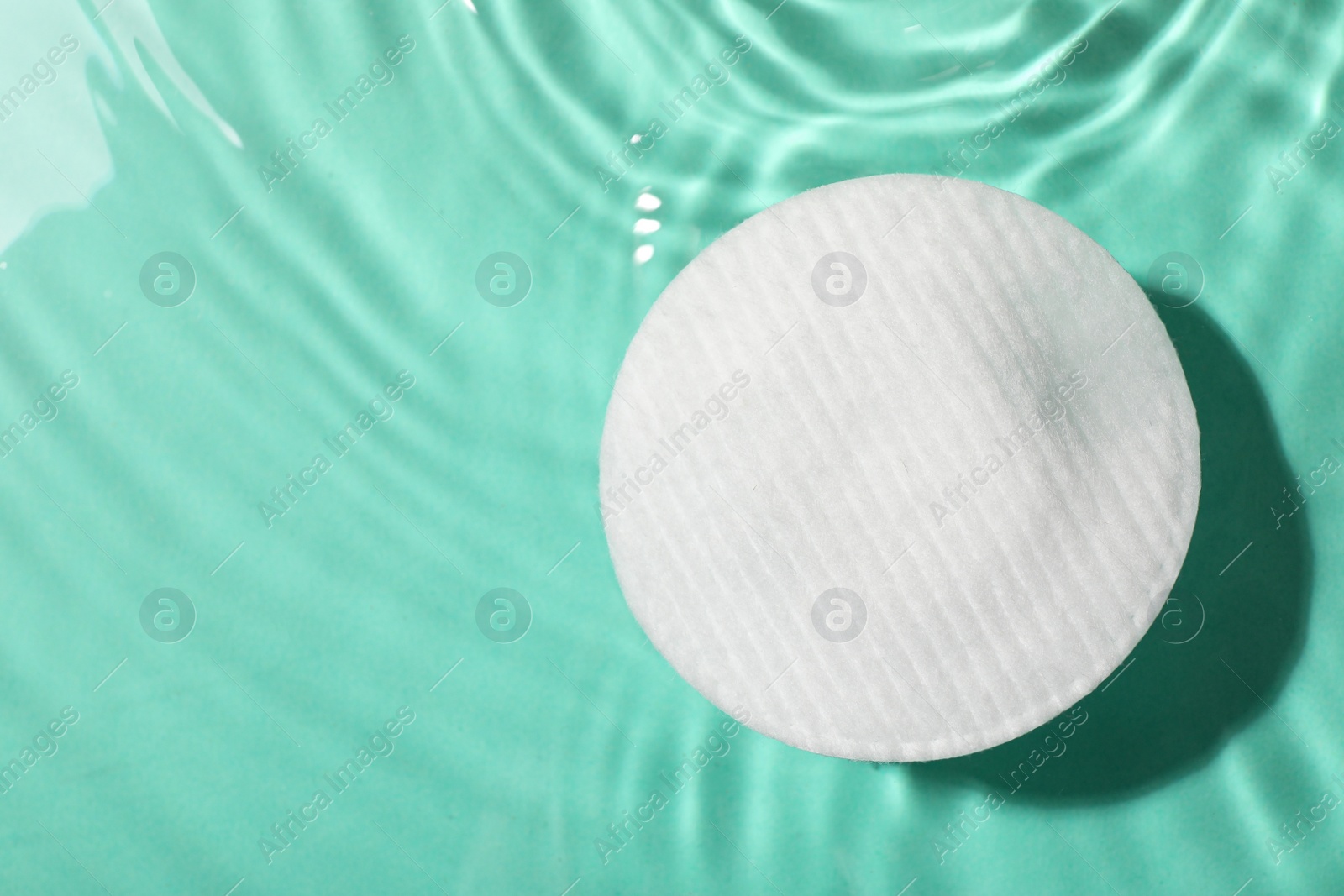 Photo of Cotton pad and micellar water on turquoise background, top view. Space for text