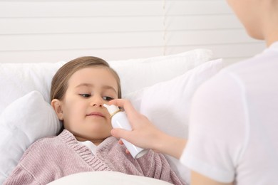 Photo of Mother using nasal spray to treat her little daughter on bed