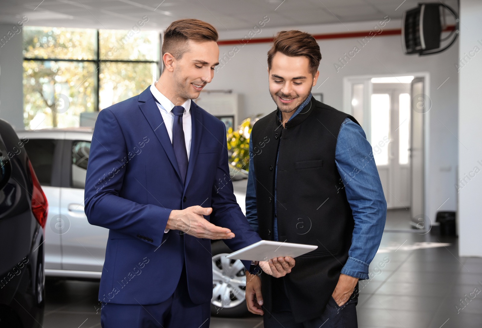 Photo of Young car salesman working with client in dealership