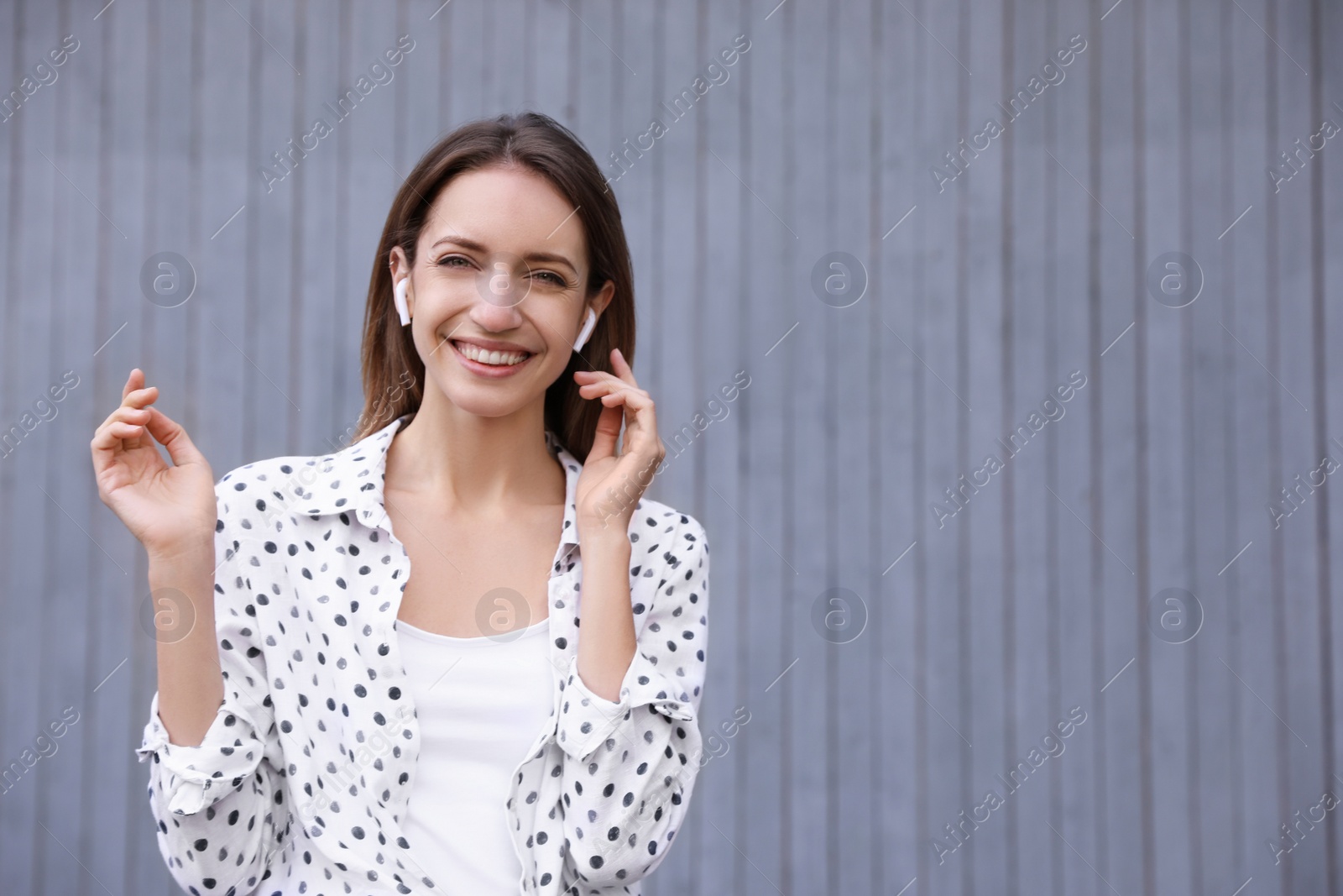 Photo of Young woman with wireless headphones listening to music near grey wall. Space for text