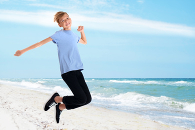 Image of Happy school boy jumping on beach near sea. Summer holidays