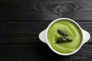 Delicious asparagus soup in bowl on black wooden table, top view. Space for text