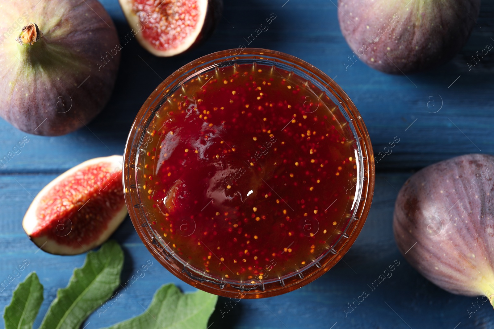 Photo of Glass bowl with tasty sweet jam and fresh figs on blue wooden table, flat lay