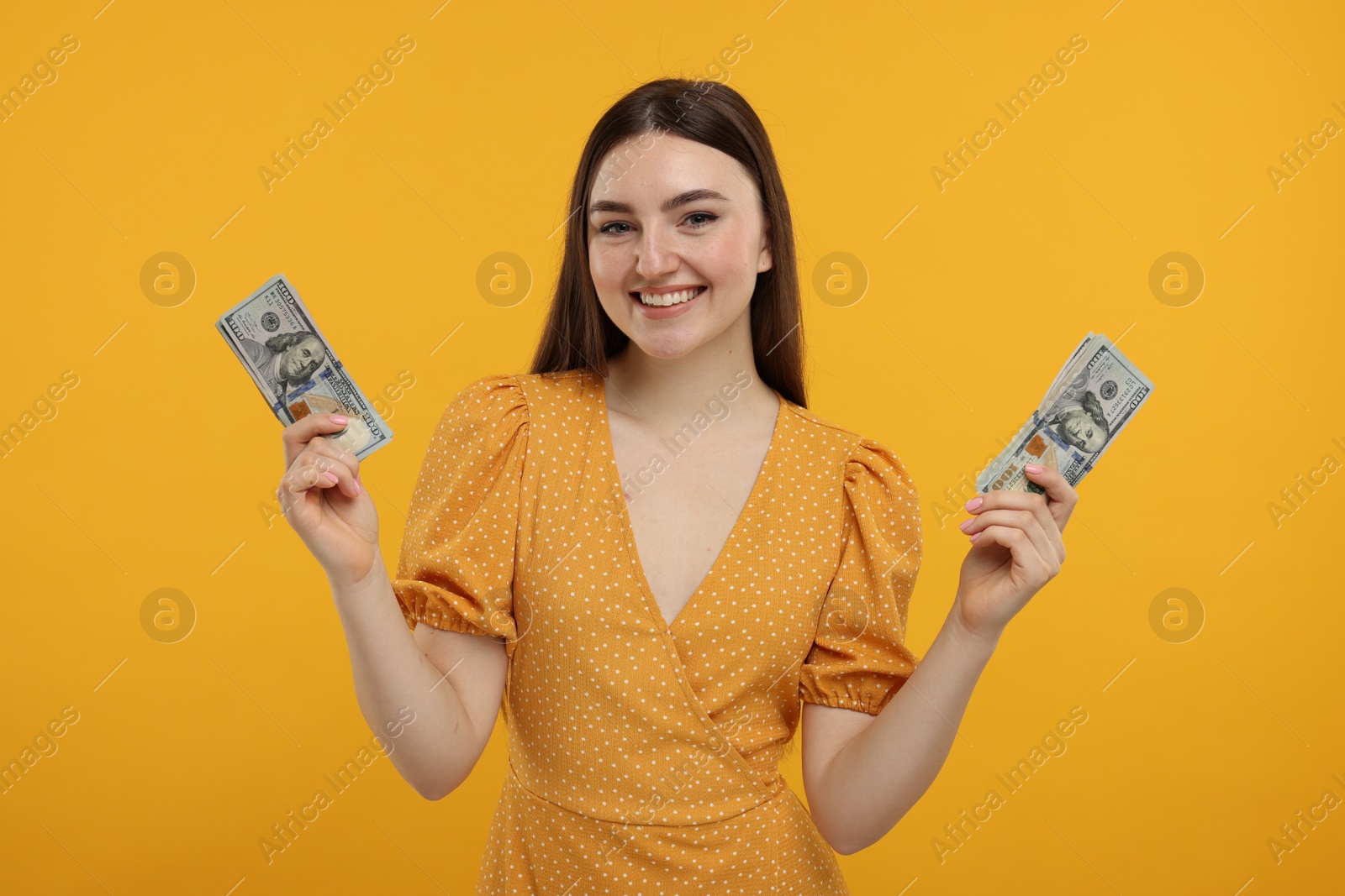 Photo of Happy woman with dollar banknotes on orange background