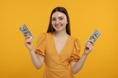 Happy woman with dollar banknotes on orange background