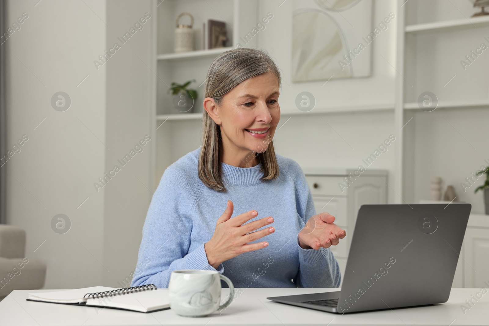 Photo of Happy woman having video chat via laptop at table indoors