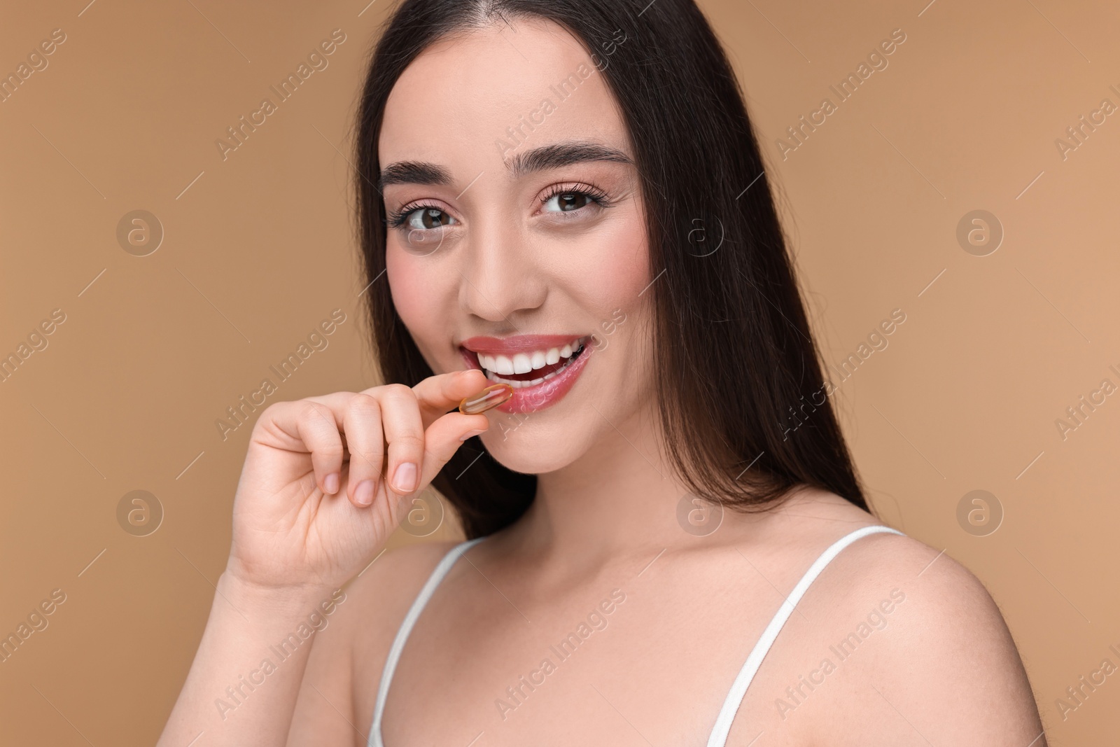 Photo of Beautiful young woman with vitamin pill on beige background