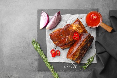 Photo of Pieces of baked pork belly served with sauce, rosemary and chili pepper on grey table, top view. Space for text