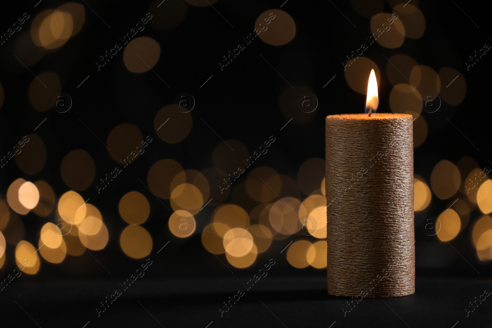 Photo of Burning gold candle against blurred lights in darkness. Space for text