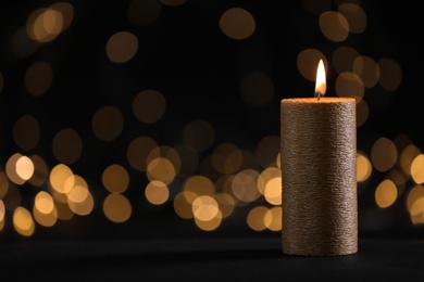 Burning gold candle against blurred lights in darkness. Space for text