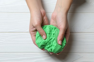 Photo of Woman playing with green kinetic sand at white wooden table, top view