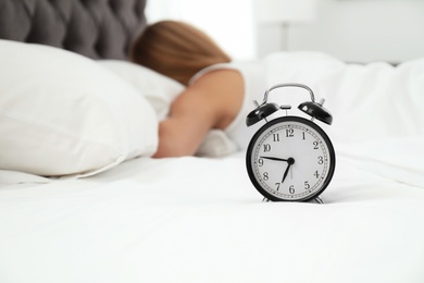 Analog alarm clock and sleepy woman in bed. Time of day