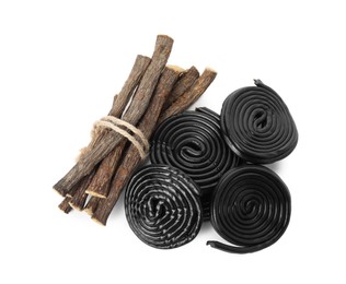 Photo of Tasty black candies and dried sticks of liquorice root on white background, top view