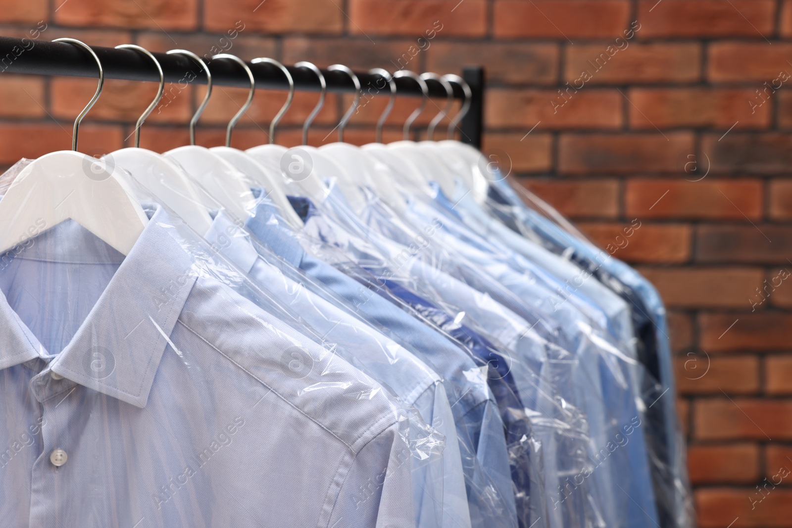 Photo of Dry-cleaning service. Many different clothes hanging on rack against brick wall, closeup