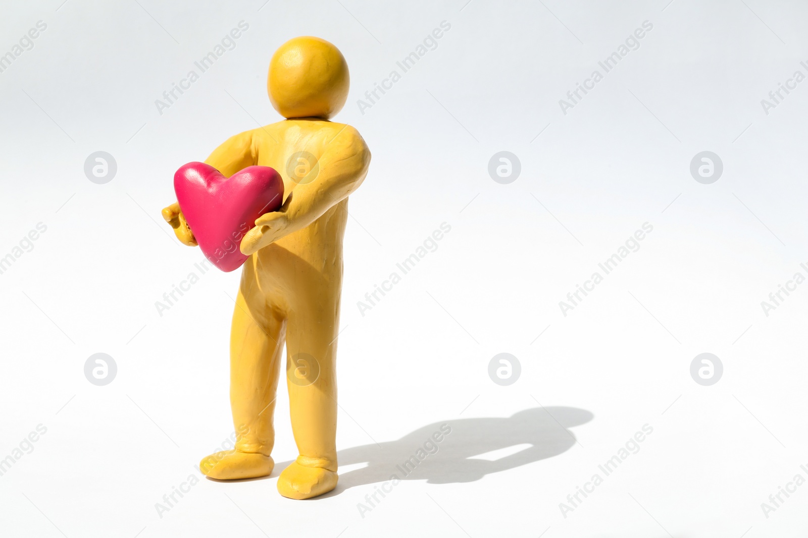 Photo of Yellow plasticine human figure with pink heart on white background, space for text