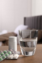 Glass of water, different pills in blisters and medical bottle on wooden table indoors