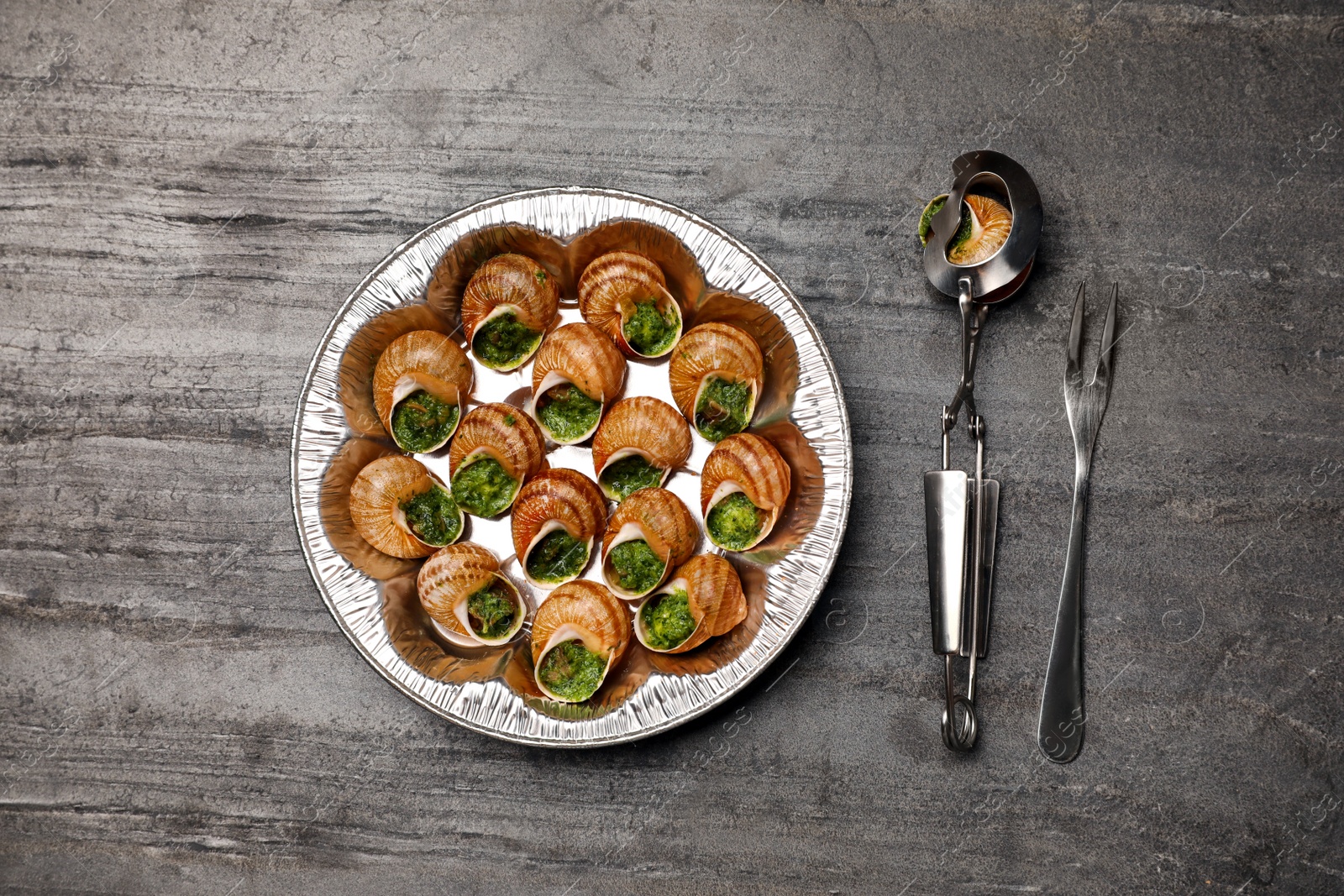 Photo of Delicious cooked snails served on grey table, flat lay