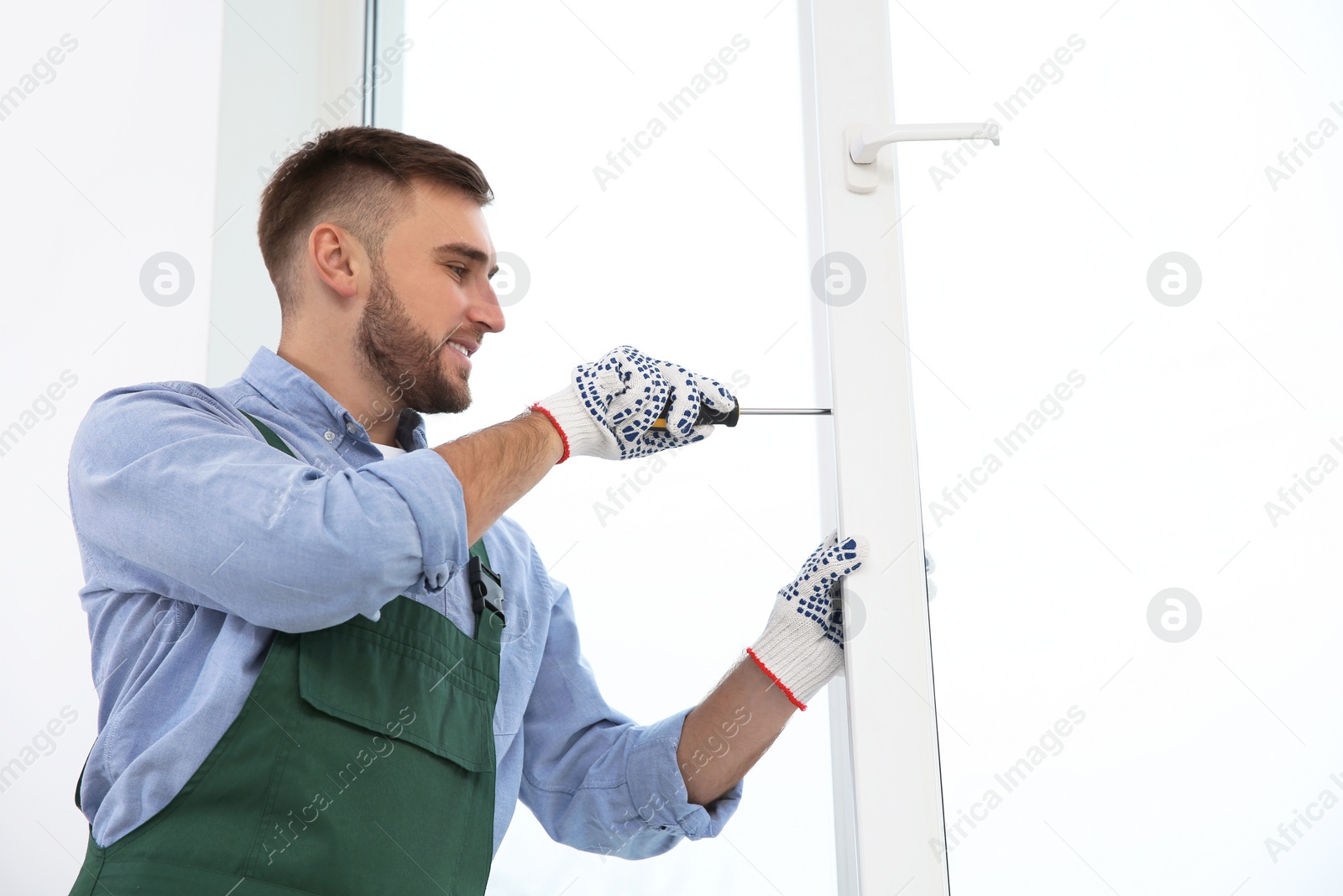 Photo of Construction worker adjusting installed window with screwdriver indoors