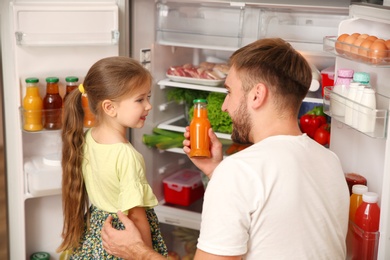 Photo of Young father with daughter taking juice from refrigerator at home