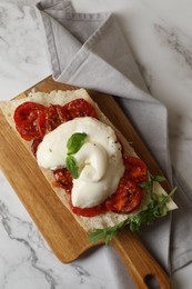 Photo of Toast with delicious burrata cheese, tomatoes and arugula on white marble table, top view