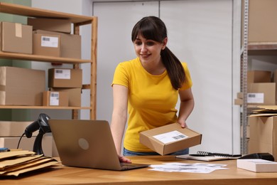 Parcel packing. Post office worker with box using laptop at wooden table indoors