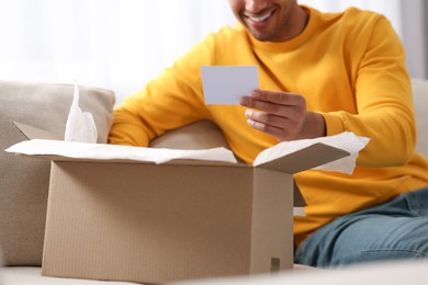 Photo of Young man holding greeting card near parcel with Christmas gift, closeup