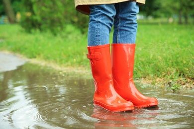 Woman with rubber boots in puddle, closeup. Rainy weather