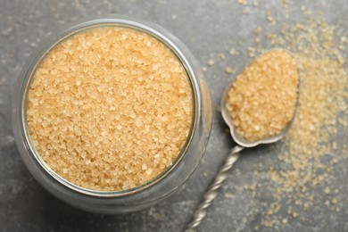 Photo of Brown sugar in bowl and spoon on grey textured table, top view