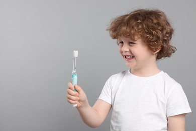 Cute little boy holding electric toothbrush on light grey background, space for text