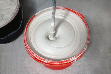 Photo of Mixing putty with electric mixer in red bucket indoors, above view
