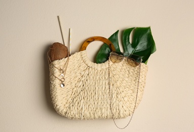 Elegant woman's straw bag with coconut, tropical leaf and accessories on beige background, top view