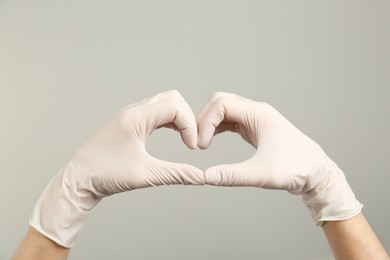 Photo of Person in medical gloves showing heart gesture on grey background, closeup of hands