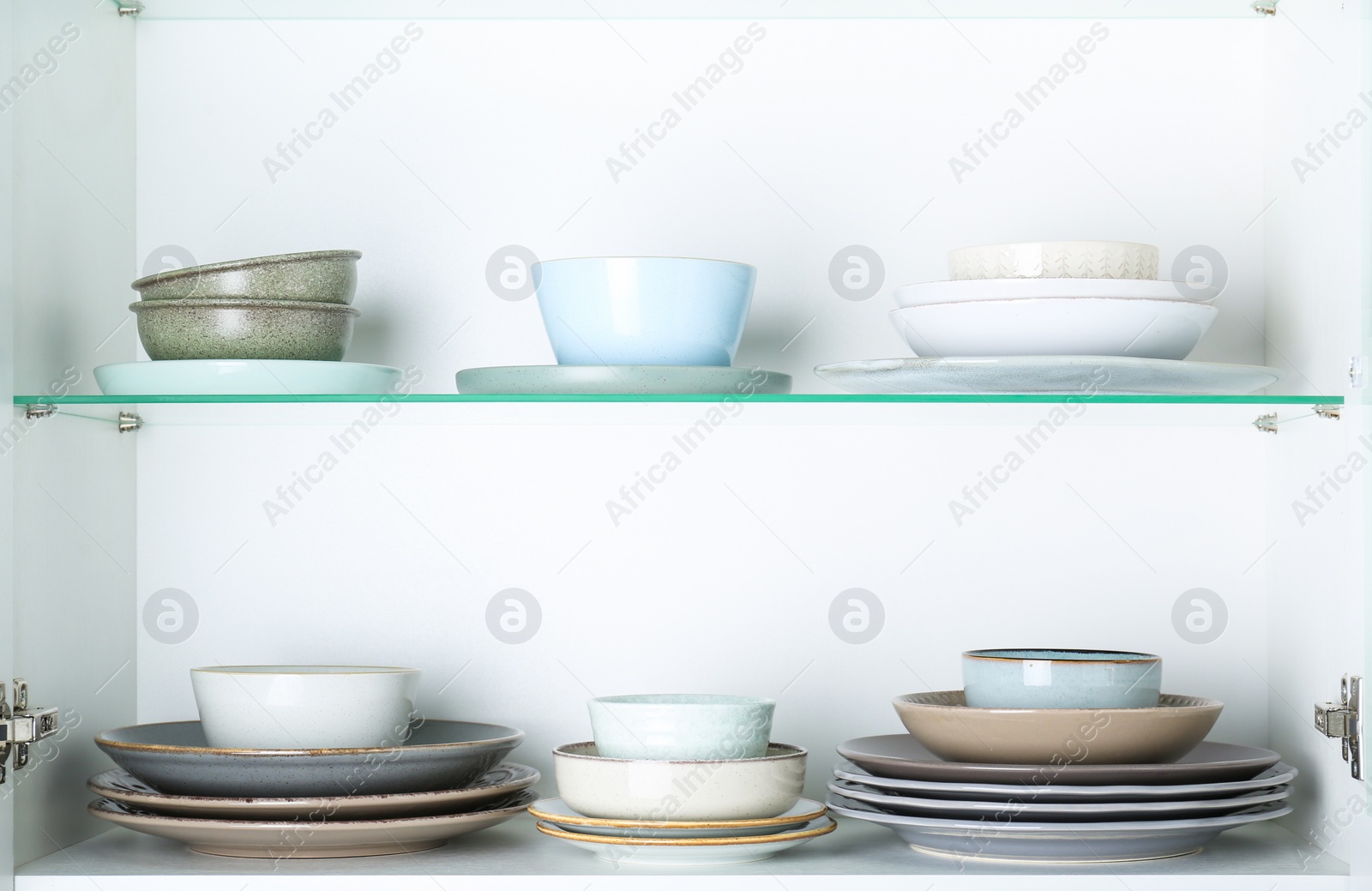 Photo of Different clean plates and bowls on shelves in cabinet