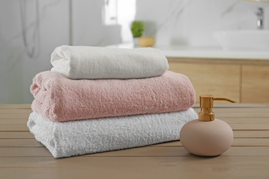 Stack of clean towels and soap dispenser on wooden table in bathroom