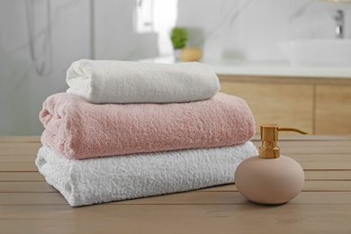 Photo of Stack of clean towels and soap dispenser on wooden table in bathroom