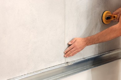 Photo of Worker with suction plate installing tile indoors, closeup