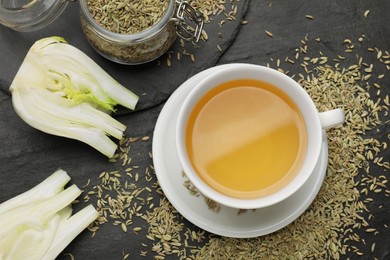 Aromatic fennel tea, seeds and fresh vegetable on black table, flat lay