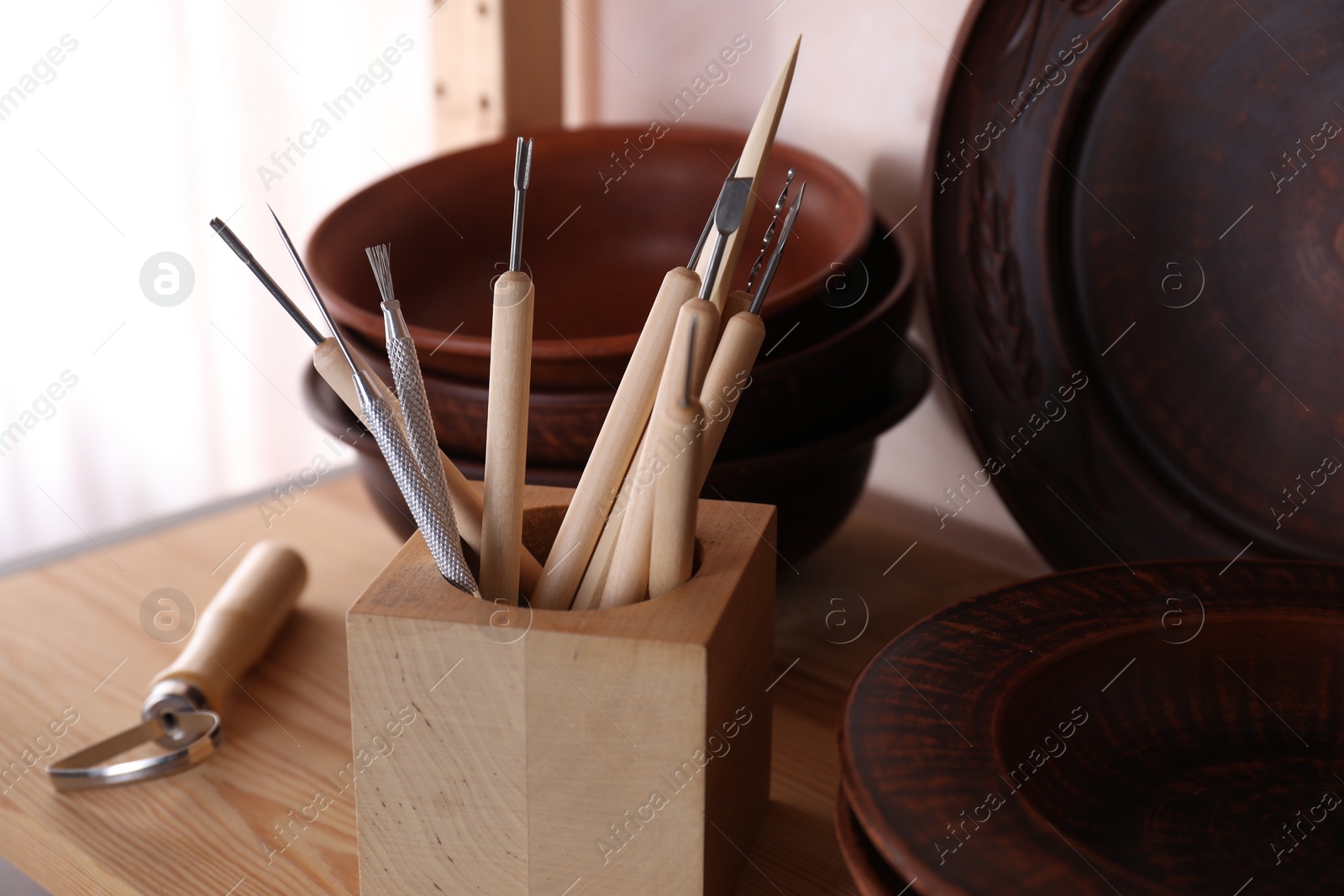 Photo of Set of different crafting tools and clay dishes on wooden table in workshop, closeup