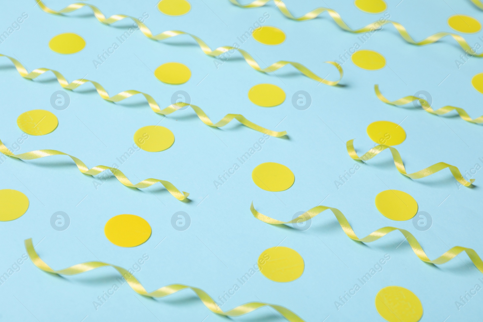 Photo of Shiny yellow serpentine streamers and confetti on light blue background