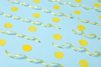 Photo of Shiny yellow serpentine streamers and confetti on light blue background