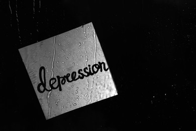 Paper sheet with word Depression on wet glass against dark background, space for text