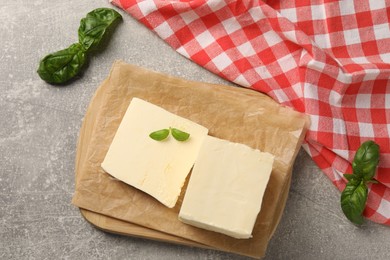 Block of tasty butter with basil on grey table, top view