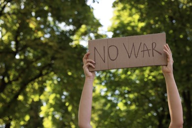 Photo of Woman holding poster with words No War in green park