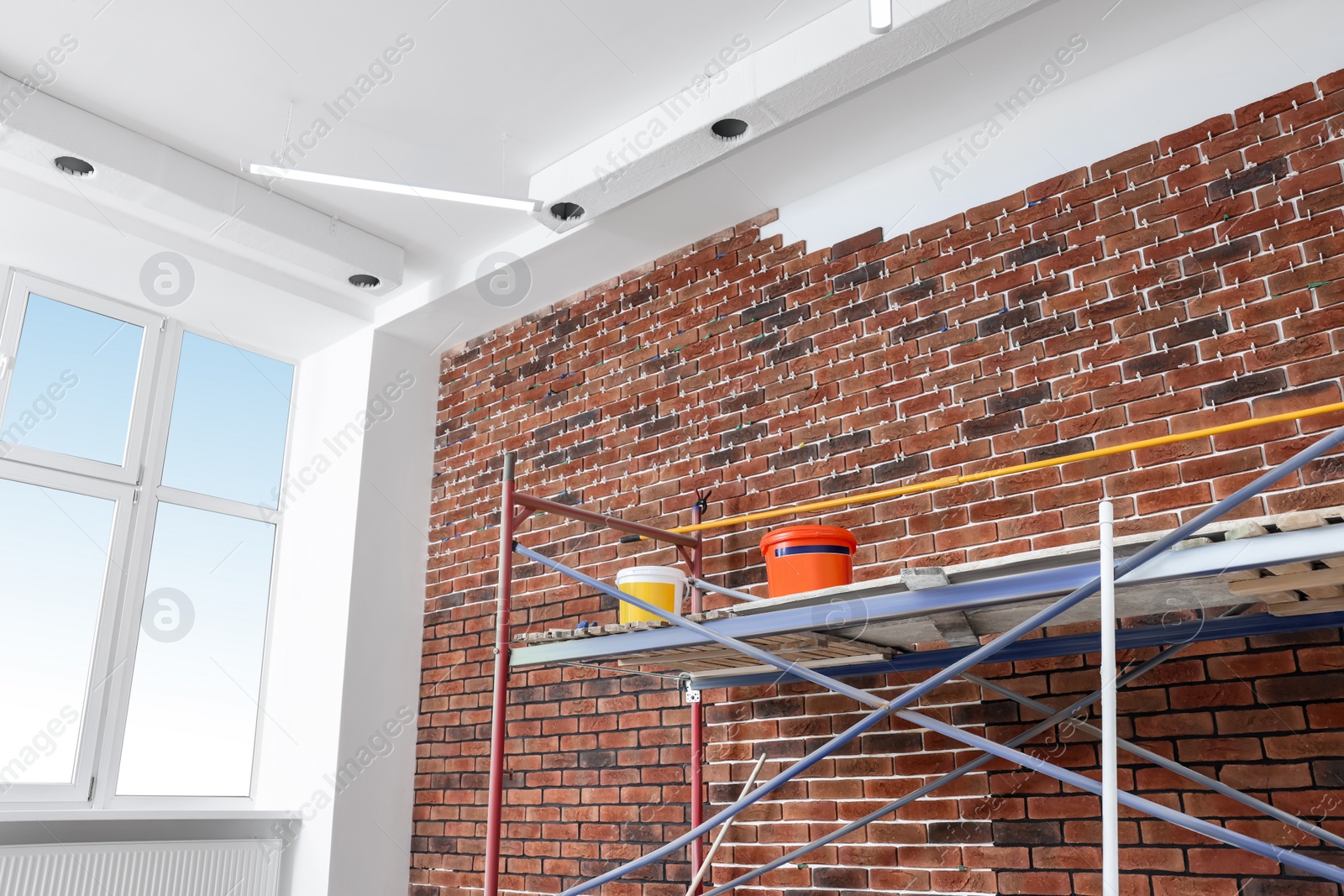 Photo of Scaffolding with equipment near brick wall in repaired room