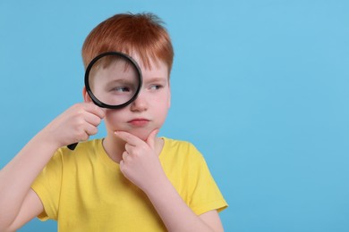 Photo of Thoughtful boy looking through magnifier glass on light blue background, space for text