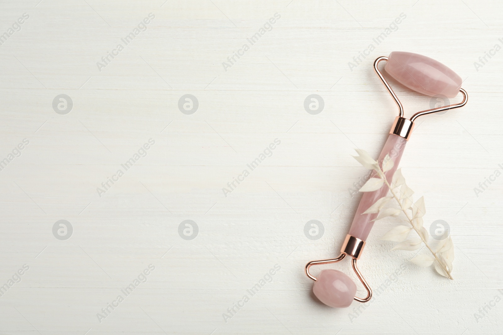 Photo of Natural rose quartz face roller and leaves on white wooden background, flat lay. Space for text